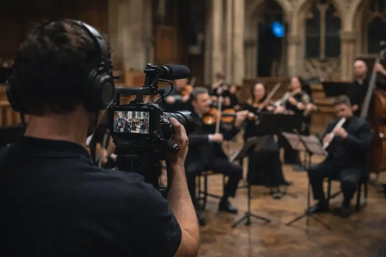 Concert videographer discreetly filming a chamber orchestra performing in a concert hall.